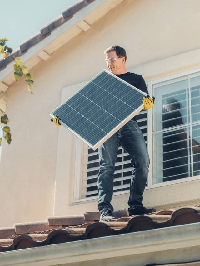 Muncitor pe casă, ținând un panou solar